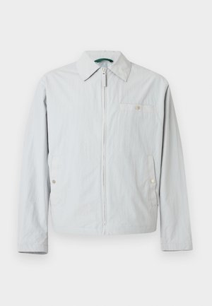 Svetlo siva jopa na zadrgo z dolgimi rokavi, ostrim ovratnikom, dvema stranskima žepoma z zaskočni gumboma ter majhnim prsnim žepom z zaskočni gumbom.