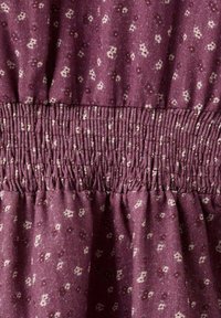 Burgundská látka s malými krémovými květinovými vzory, s nařaseným pasem a jemnou strukturou; nabíraní vytváří uvolněný střih.