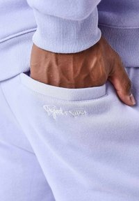 Sudadera de color púrpura claro con puños acanalados y un bolsillo lateral, con "Project" bordado en blanco en la zona del bolsillo.