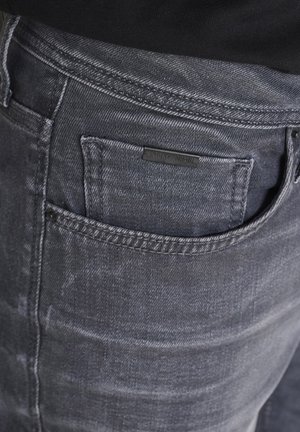 Sive traperice s blagim izbleđenim finišom, s leđnom džepom i malom crnom etiketom s nazivom branda.