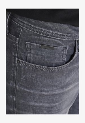 Sive traperice s blagim izbleđenim finišom, s leđnom džepom i malom crnom etiketom s nazivom branda.