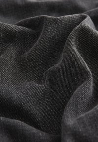 Primo piano di tessuto morbido e spiegazzato di colore grigio scuro con una sottile trama diagonale che crea pieghe e ombre delicate.