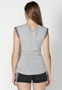 Sivý krátky rukáv s naťahovacími detailmi po bokoch a kontrastným čiernym lemom na rukávoch, spárovaný s čiernymi šortkami. Hladká, ľahká tkanina.