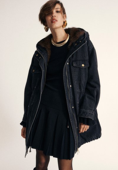 Denim parka s kožušinou podšitým kapucňou, zipsovým zapínaním, zlatými detailami, bočnými vreckami a voľným strihom, skombinovaný s čiernym pleteným sveterom a skladanou sukňou.
