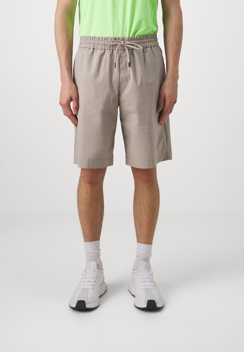 Bežid lühikesed püksid elastse vöökoht ja nööriga, kangas on sileda tekstuuriga; kantud valgete sneakers'ite ja lühikeste sokkidega.
