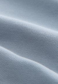 Světlomodrá látka s texturovaným vzorem tkaní, zobrazující měkké záhyby a jemný lesk, což naznačuje lehký a prodyšný materiál.