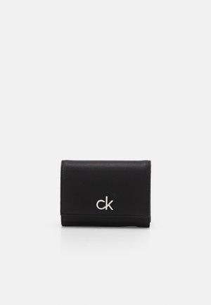 Portefeuille en cuir noir avec logo "ck" argenté centré sur le rabat avant, présenté sur un fond blanc uni.
