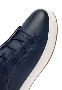 Granatowy skórzany sneaker z białą gumową podeszwą, brązową zewnętrzną krawędzią i granatowymi sznurowadłami przewleczonymi przez przeszywane dziurki.