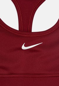 Kardinalni športni modrček z gladko teksturo, ki ima bel Nike logotip, hrbtni del v dizajnu racerback in podrobno šivanje vzdolž robov.
