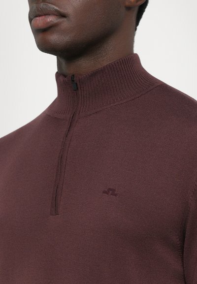 Sweat à zip marron avec un col haut, texture côtelée et logo discret sur la poitrine. Équipé d'un zip demi-long pour un ajustement réglable.