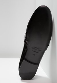 Chaussure en cuir verni noir avec un design élégant, une finition lisse, un bout arrondi, et une étiquette embossée sur la semelle indiquant la taille 41.