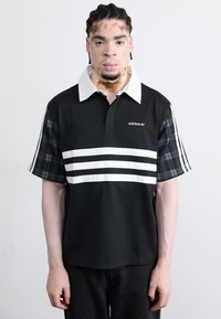 Black polo shirt with white stripes across the chest, a white collar, and plaid patterned sleeves. Features Adidas logo on the front.