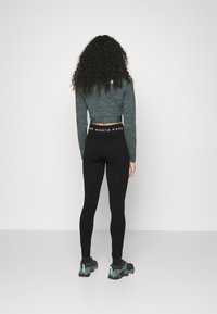 Leggings neri abbinati a un top lungo a maniche corte verde scuro con tessuto testurizzato e un elastico in vita, indossati con sneakers nere e turchesi.