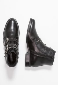 Černé kožené kotníkové boty s hladkým povrchem, které mají dva přezkové pásky a hřebíkované detaily. Bo�ční zip a nízký stohovaný podpatek.
