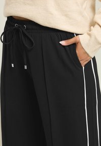 Svarta träningsoverallsbyxor med dragsko i midjan, med vita sidostrecker, mjuk textur och sidofickor.