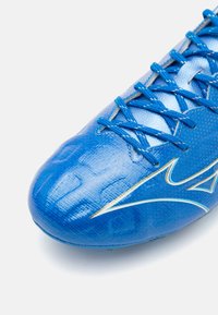 Blauer Fußballschuh mit glänzender Textur, strukturiertem Muster und blauen Schnürsenkeln. Auffälliges Logo in einer kontrastierenden Farbe an der Seite.