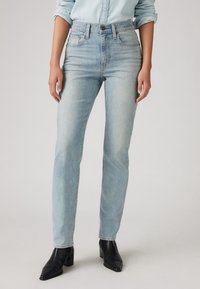Light blue denim jeans with a high waist, straight leg design, minimal distressing, and a slightly faded texture. Paired with black heeled boots.