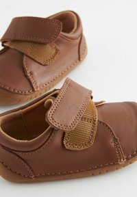 Chaussures en cuir marron avec une sangle Velcro, accents en tissu marron texturé, forme arrondie et semelles en caoutchouc, adaptées aux tout-petits.