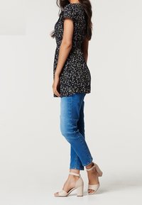 Blommigt top i marinblått med korta ärmar, ihop med blå slim-fit jeans och beiga klacksandaler. Släta texturer och figurnära design.