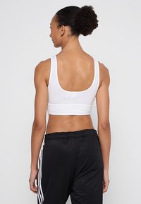 Baltas sportinis liemenėlė su aukšta nugara, plačiomis petnešėlėmis ir elastine juosta. Derinama su lengvomis juodomis sportinėmis kelnėmis su baltomis šoninėmis juostomis.