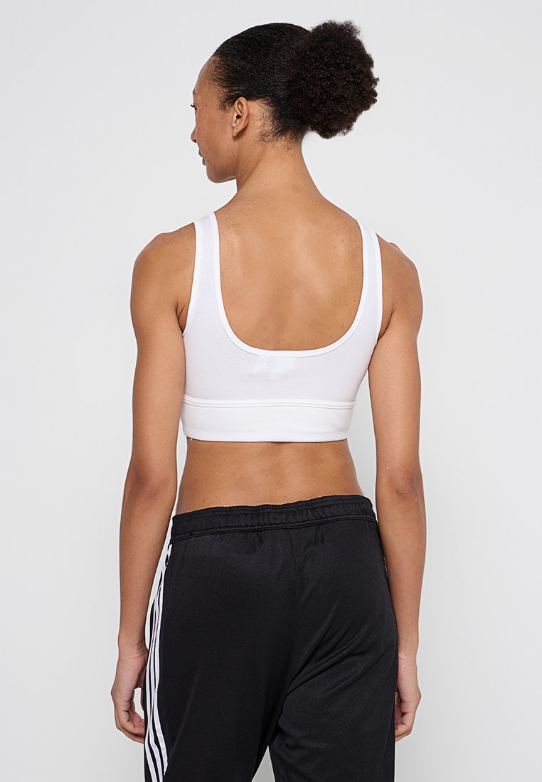Weißer Sport-BH mit hohem Rücken, breiten Trägern und elastischem Bund. Kombiniert mit leichten schwarzen Trainingshosen mit weißen Seitenstreifen.