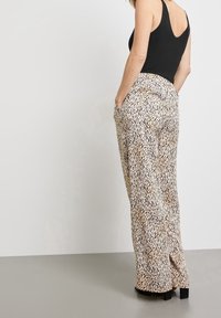 Pantalons ample taille haute en beige avec des motifs abstraits noirs, dotés de poches latérales et d'un design droit.