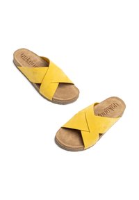 Sandalias de ante amarillas con tiras cruzadas, suela de corcho y una plantilla beige con marca impresa. Diseño plano y punta abierta.