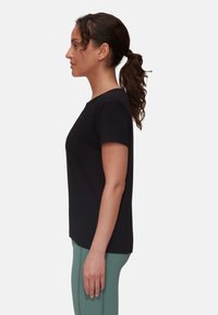 T-shirt nero a maniche corte con collo rotondo, indossato con leggings verdi a vita alta. Tessuto morbido con un design aderente.
