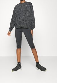 Persona vestida con sudadera de leopardo en negro y gris, leggings cortos negros, calcetines negros y zapatillas Nike negras con suelas blancas.