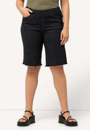 Mustat denim-bermuda-shortsit, joissa on joustava vyötärö, revennyt helma ja etutaskut, yhdistettyinä vihreään paitaan ja mustiin korkokenkiin.