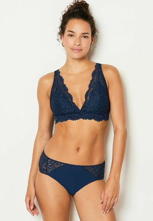 Bralette en dentelle marine avec un décolleté en V profond et des bords festonnés, associé à un string de bikini assorti avec des accents en dentelle sur les côtés.