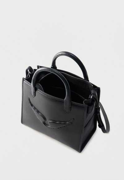 Μαύρη δερμάτινη τσάντα χειρός με δύο λαβές, μεγάλο κεντητό λογότυπο στη μία πλευρά και ανοιχτή κορυφή που δείχνει ένα εσωτερικό διαμέρισμα με φερμουάρ.