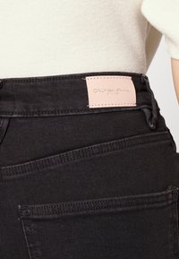 Svarta denimjeans med en rosa läderetikett på midjan med präglat varumärkesnamn. Slät textur och standardficka design.