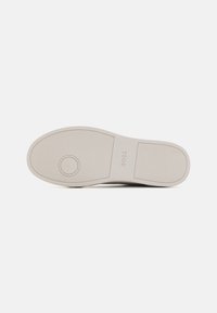 Suola della scarpa in gomma bianca sporca con una texture liscia, dettaglio del logo circolare e design a motivo per garantire aderenza.