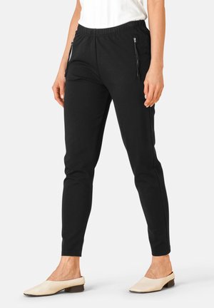 Sorte joggerbukser med elastisk talje, sidelommer med lynlås, en tætsiddende pasform og en glat stofstruktur, parret med beige slip-on sko.