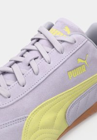 Light purple suede sneaker with yellow accents, featuring lace-up design, textured side panel, and brown rubber outsole. PUMA logo displayed.