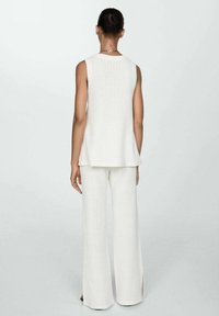 Biały dziergany top bez rękawów o luźnym kroju, zestawiony z pasującymi szerokimi spodniami z bocznymi rozcięciami. Teksturowana tkanina, minimalistyczny design.