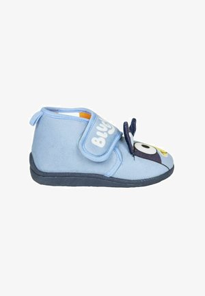 Zapatilla de tela de color azul claro con una correa de velcro, punta redondeada y diseño de personaje de dibujos animados en la parte frontal. Suela negra y textura suave.