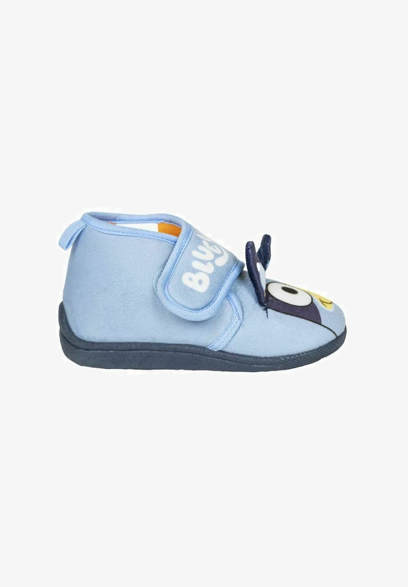 Zapatilla de tela de color azul claro con una correa de velcro, punta redondeada y diseño de personaje de dibujos animados en la parte frontal. Suela negra y textura suave.