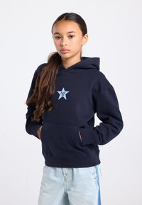 Donkerblauwe hoodie met een zak aan de voorkant, voorzien van een lichtblauwe stergraphic en de tekst "Lucky Me." Gemaakt van zachte stof met geribbelde manchetten.