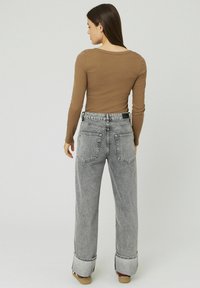 Haut marron à manches longues associé à un pantalon en jean gris taille haute et à jambes larges, avec des ourlets retroussés et des détails distincts sur les poches arrière.