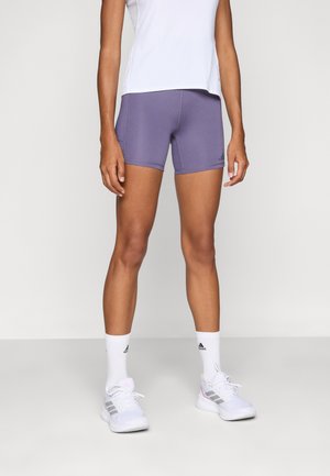 Shorts atletici violeti, confecționați dintr-un material elastic, cu un design ajustat și cusături contrastante. Purtați cu un top alb și pantofi sport.