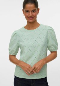 Blusa verde chiaro a maniche corte con spalle a palloncino, caratterizzata da un motivo a rombi in eyelet e da un tessuto leggermente testurizzato.
