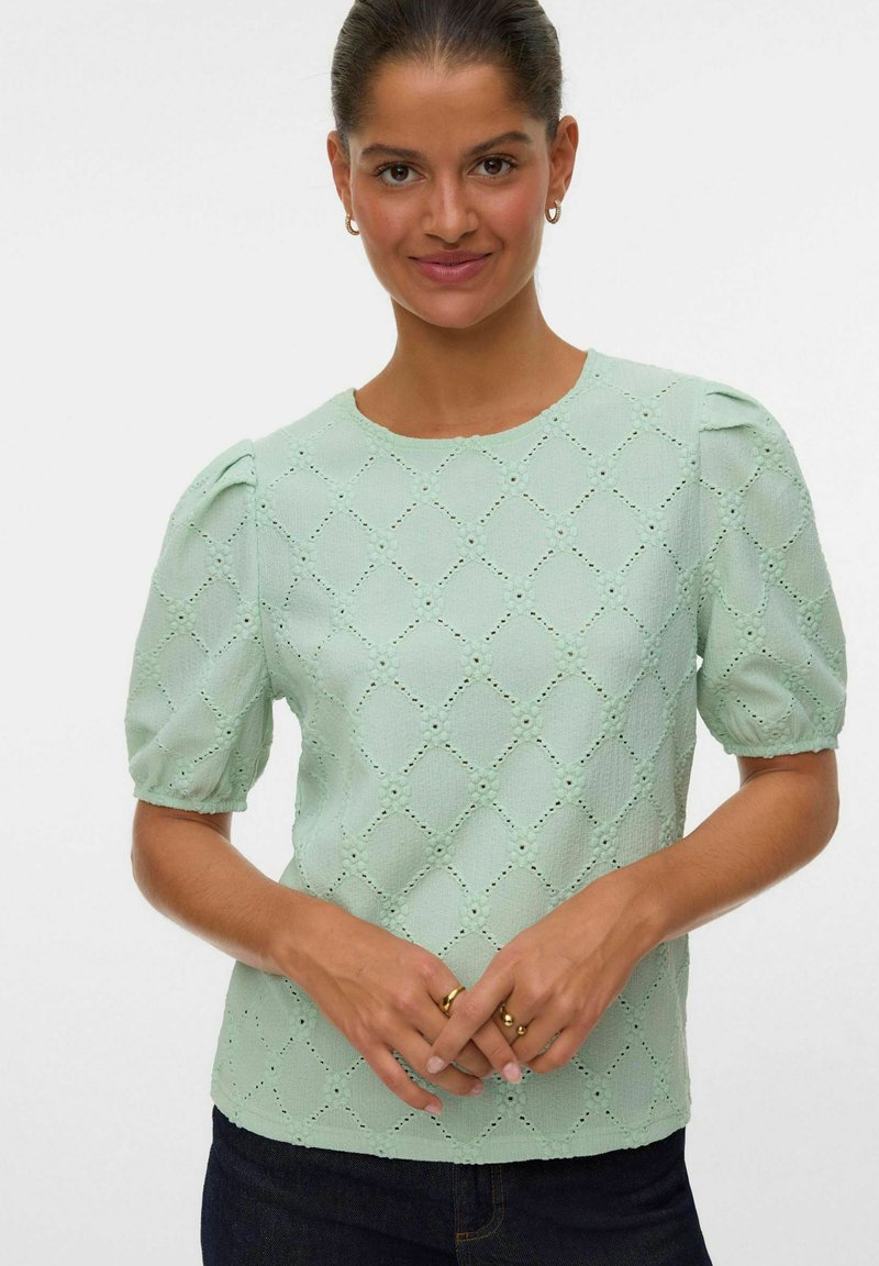 Blusa verde chiaro a maniche corte con spalle a palloncino, caratterizzata da un motivo a rombi in eyelet e da un tessuto leggermente testurizzato.