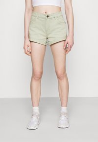 Vaaleanvihreät farkkushortsit, joissa on korkea vyötärö, käännetyt lahkeet, etutaskut ja yksi nappisulku. Yhdistetty valkoisiin lenkkareihin ja sukkiin.