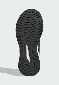 Schwarze Gummisohle eines Sportschuhs mit tiefen Profilen, geschwungener Form und einem weißen Akzent. Enthält ein dreieckiges Logo und ein Detail "schmutzfrei".