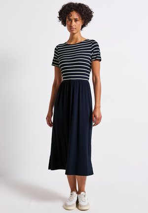 Gestreepte midi-jurk in marineblauw en wit, korte mouwen, ronde halslijn, elastische taille, vloeiende stof, gecombineerd met witte sneakers.