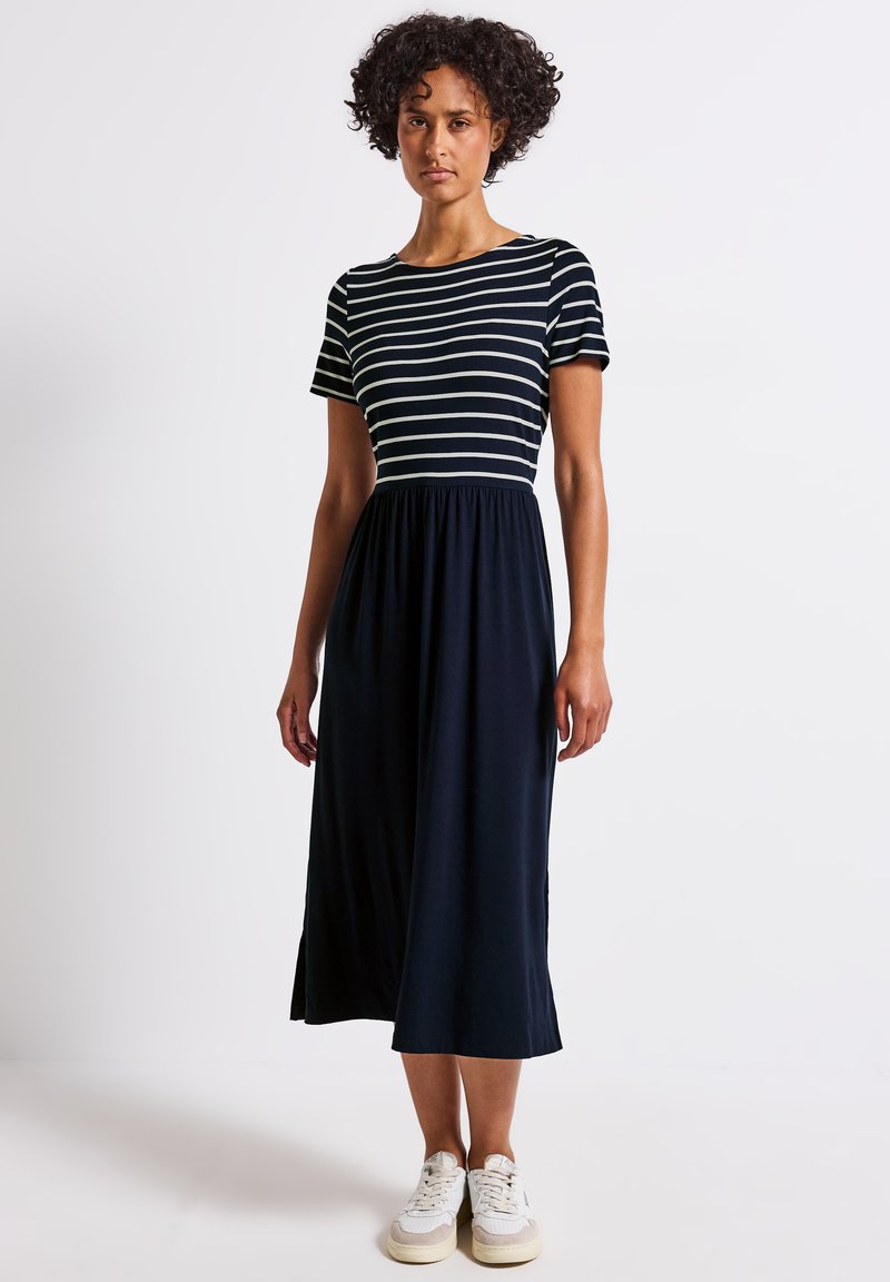 Vestido midi a rayas en azul marino y blanco, con mangas cortas, cuello redondo, cintura elástica, tejido fluido, combinado con deportivas blancas.