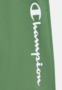 Joggeurs verts en mélange de coton doux, arborant un logo "Champion" blanc bien visible verticalement sur le côté.