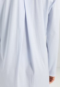 Jasnoniebieska bluzka z długim rękawem o luźnym kroju, z plisą z tyłu i miękką, gładką teksturą. Prosty i minimalistyczny design.